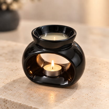 Black ceramic wax melt burner lit with a tealight and pale melted wax on a cream stone surface.