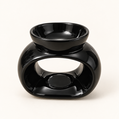 Front view of a glossy black oval ceramic wax melt burner on a warm cream background.